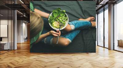 Green vegan breakfast meal in bowl with spinach, arugula, avocado, seeds and sprouts. Girl in jeans holding fork with knees and hands visible, top view. Clean eating, detox, vegetarian food concept Wall mural