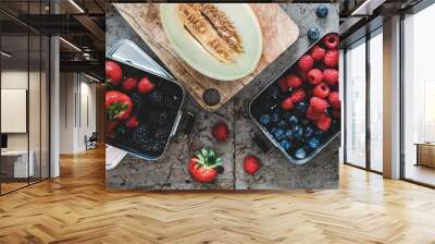 Healthy summer vegan lunch. Flat-lay of fresh seasonal strawberries, raspberries, blueberries, blackberries in metal lunchboxes and melon over rough grey background, top view. Vegan, vegetarian food Wall mural