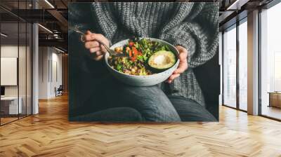 Healthy vegetarian dinner. Woman in grey jeans and sweater eating fresh salad, avocado half, grains, beans, roasted vegetables from Buddha bowl. Superfood, clean eating, dieting food concept Wall mural