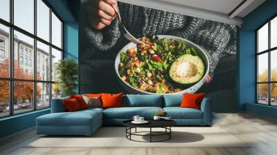 Healthy vegetarian dinner. Woman in jeans and sweater eating fresh salad, avocado half, grains, beans, roasted vegetables from Buddha bowl, square crop. Superfood, clean eating, dieting food concept Wall mural