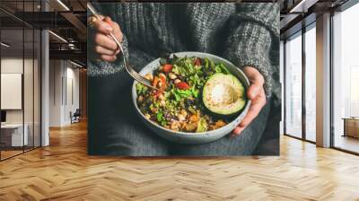 Healthy vegetarian dinner. Woman in jeans and warm sweater holding bowl with fresh salad, avocado, grains, beans, roasted vegetables, close-up. Superfood, clean eating, vegan, dieting food concept Wall mural