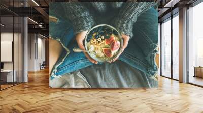 Healthy winter breakfast in bed. Woman in sweater and jeans holding rice coconut porridge with figs, berries, hazelnuts, top view, wide composition. Clean eating, vegetarian, comfort food concept Wall mural