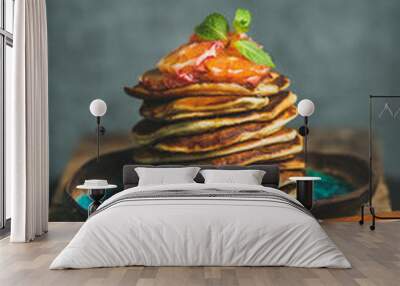 Homemade pancakes with honey, bloody orange slices and mint leaves for breakfast on blue ceramic plate over rustic wooden board, grey plywood wall at background, selective focus, copy space Wall mural