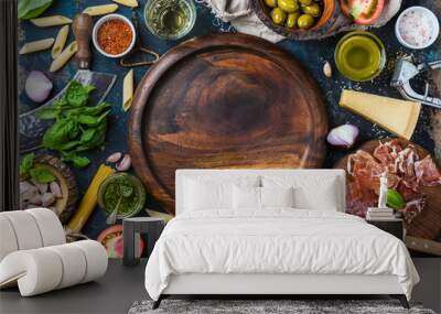 Italian food cooking ingredients on dark plywood background with round wooden tray in center, top view, copy space, horizontal composition Wall mural