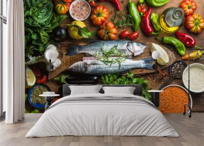 Raw uncooked seabass fish with vegetables, grains, herbs and spices on chopping board over rustic wooden background Wall mural