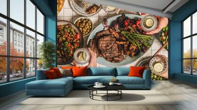 Summer barbeque party. Flat-lay of table with grilled meat, vegetables, salad, roasted potato and peoples hands with glasses of lemon water over white tablecloth, top view, wide composition Wall mural