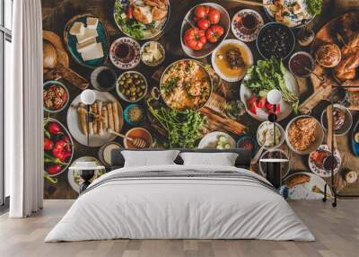 Turkish breakfast table. Flat-lay of fresh pastries, vegetables, greens, olives, cheeses, fried eggs, jams, honey, tea in copper pot and tulip glasses, top view. Middle Eastern meal Wall mural