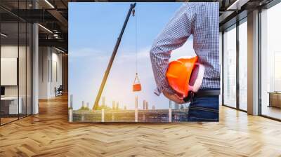 engineer holding yellow safety helmet in building construction site with crane Wall mural