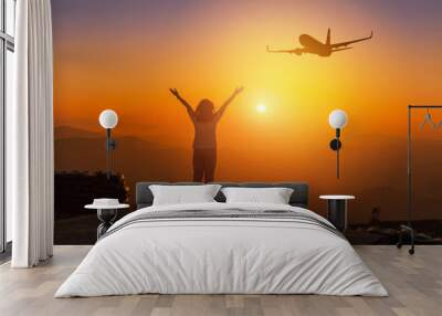 Silhouette back of woman stand raising up two arm celebrate enjoying on high cliff mountain while airplane flying in sunset time, freedom destination travel concept  Wall mural