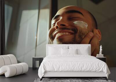 Young bearded man applying anti-aging moisturiser lotion for skin care and dryness, guy smiling in the mirror, copy space Wall mural