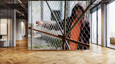 Asian male teenager puts his hand on the metal fence around detention center of his village because he was detained for inappropriate behavior, freedom and detention of young people concept. Wall mural