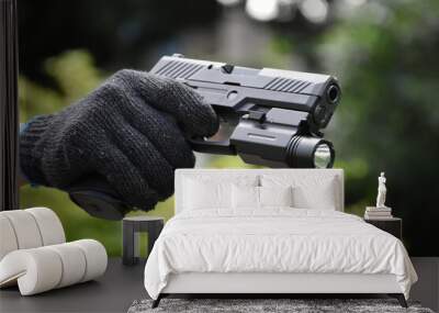 Automatic 9mm pistol which has flashlight under the muzzle holding in hand and ready to shoot, natural blurred background. Wall mural