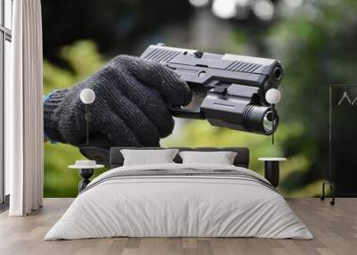 Automatic 9mm pistol which has flashlight under the muzzle holding in hand and ready to shoot, natural blurred background. Wall mural