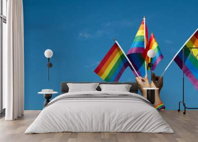 Rainbow flags showing in hands against clear bluesky, copy space, concept for calling all people to support and respcet the genger diversity, human rights and to celebrate lgbtq+ in pride month. Wall mural