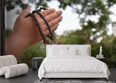 Wooden cross and wooden rosary are held in hands of young asian Catholic prayer while praying in the temple park area. Wall mural