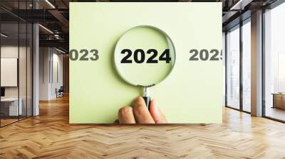 A magnifier zooming in on the 2024 icon, the target business for the upcoming year. It represents planning, investment, and innovation ideas transitioning from the end of 2023 to the new year concept. Wall mural