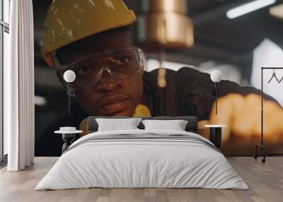 American industrial black young worker man with yellow helmet and ear protection manual rotating on drill machine In order to penetrate workpiece, Engineer at work in industry factory. Wall mural