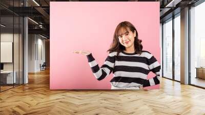 Asian happy portrait beautiful cute young woman smile standing presenting product holding something on palm away side, studio shot isolated on pink background with copy space, female show hand gesture Wall mural