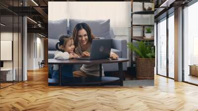 Asian young mother with laptop computer teaching her kid to learn or study online in living room at home, Mum and little preschool daughter learning online on computer, family homeschooling online Wall mural