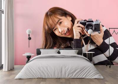 Attractive energetic happy Asian portrait beautiful young woman smiling photographer taking a picture and looking viewfinder on retro vintage photo camera ready to shoot isolated on pink background Wall mural