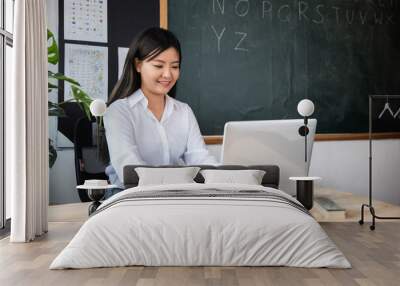 Back to school. Smiling female using computer sitting at school table, Portrait of young woman teacher with laptop at desk in classroom, Online education and learning concept Wall mural