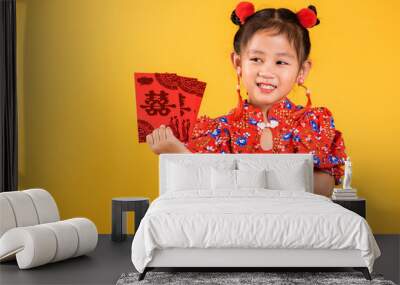 Chinese New Year. Happy Asian Chinese little girl smile wear red cheongsam qipao hold angpao red packet monetary gift, Portrait child in traditional dress, studio short isolated on yellow background Wall mural