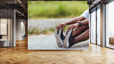 Close up Asian young athlete sport runner black man wear watch he sitting pull toe feet stretching legs and knee before running at outdoor street health park, healthy exercise before workout concept Wall mural