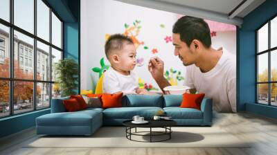 Father acting Mom feeding his son baby 1 year old on chair Wall mural