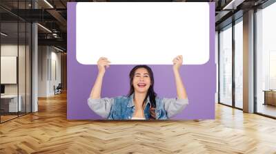 Happy Asian beautiful young woman smiling excited wear denims hold empty speech bubble sign, Portrait female posing show up for your idea looking at camera, studio shot isolated on purple background Wall mural