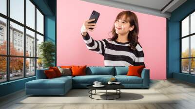 Happy Asian portrait beautiful cute young woman smiling excited making selfie photo, video call on smartphone studio shot isolated on pink background, female hold mobile phone raise hand say hello Wall mural