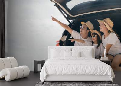 Happy Family Day. Family travel in holiday at sea beach, Dad, mom, daughter enjoy road trip sitting on back car and pointing finger out, people having fun in summer vacation on beach with automobile Wall mural