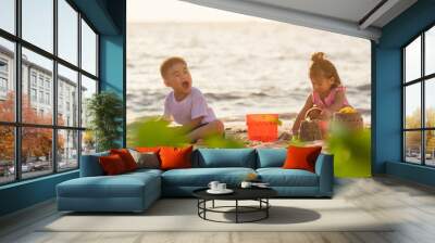 Happy fun two Asian children cute little boy and girl brother and sister family playing sand with toy sand tools at a tropical sea beach in holiday summer on sunset time, tourist trip concept Wall mural