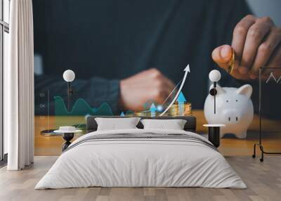 Investment strategy - businessman hand putting coins in a piggy bank with a background of stock market charts and graphs. Saving for future growth and financial security. Wall mural