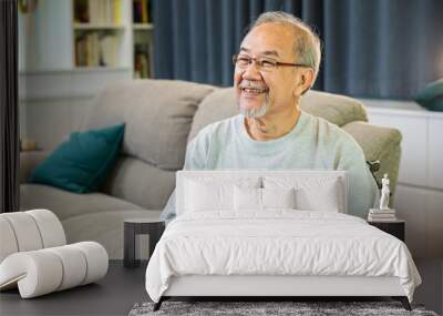 Portrait Asian old man alone relaxing on comfortable couch in cozy living room at home, happy smiling positive older senior male laughing at funny joke and thinking about good future Wall mural