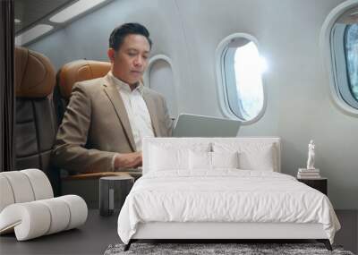 Professional Asian businessman working with notebook computer while sitting inside an airplane Wall mural