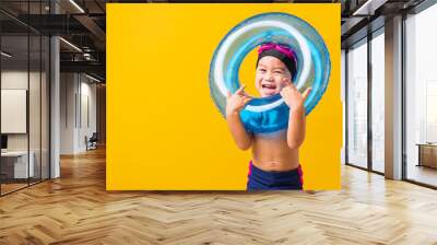 Summer vacation concept, Portrait Asian happy cute little child boy wear goggles and swimsuit hold blue inflatable ring, Kid having fun on summer vacation, studio shot isolated yellow background Wall mural