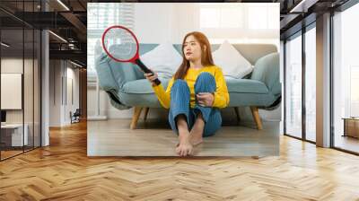 Woman killing mosquitoes hand holding fly swatter like weapon in living room at home, Asian young female sitting floor using mosquito swatter or electric net racket, technology insect killer Wall mural