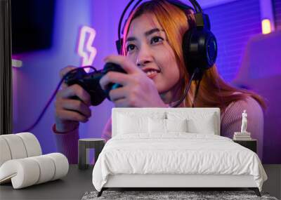 You win. Gamer using joystick controller plays online video game with computer neon lights she winning, woman wear gaming headphones playing live stream esports games console at home celebrating win Wall mural