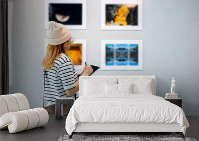 Young person at photo frame write digital book leaning against at show exhibit artwork gallery, Asian woman holding tablet at art gallery collection in front framed paintings looking pictures on wall Wall mural