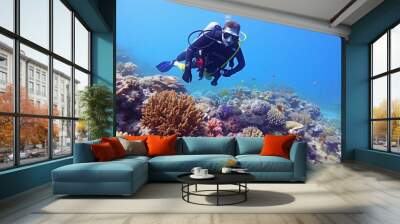 Female scuba diver swimming among colorful coral reef underwater in tropical sea Wall mural