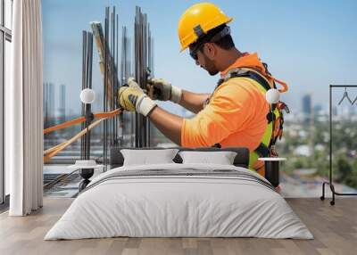 A construction worker secures rebar on a building site, showcasing safety gear and city skyline under a clear blue sky. Wall mural