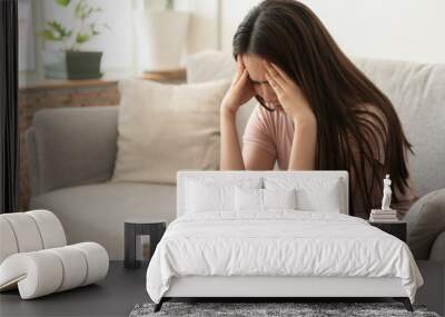 Asian woman are holding their hands to the head in pain on the sofa at home, Young women have severe headaches from migraines, Health and illness concept Wall mural