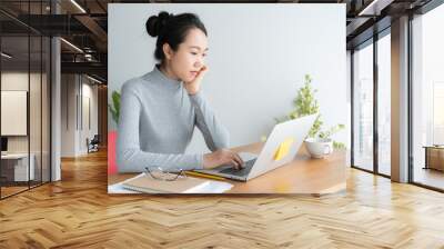 Young asian woman working on laptop in the home office desk, And sit at table resting chin on hand. Wall mural