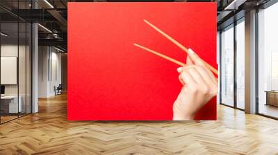 Creative image of wooden chopsticks in female hand on red background. Japanese and chinese food with copy space Wall mural