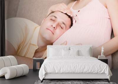 man is listening to his beautiful pregnant wife tummy and smiling at the home Wall mural