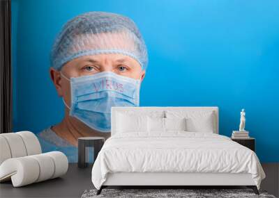 Portrait of man wearing medical uniform and mask with virus word at blue background. Protect your health. Coronavirus concept with copy space Wall mural