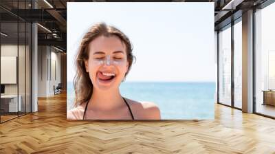 Tanned woman protects her face with sun cream from sunburn at the beach Wall mural