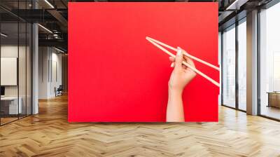 Woman's hand holding chopsticks on red background. Chinese food concept with empty space for your design Wall mural