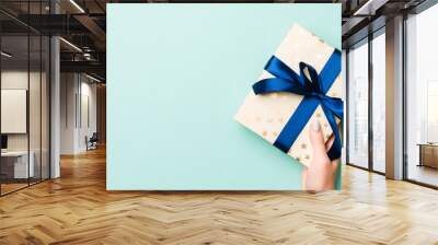 Woman hands give wrapped christmas or other holiday handmade present in colored paper. Present box, decoration of gift on Blue table, top view with copy space Wall mural