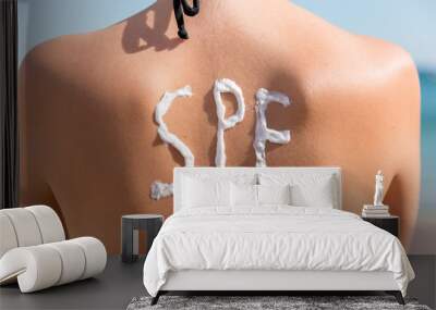 Young girl has spf word on her back made of sun cream at the beach. Sun protection factor concept Wall mural